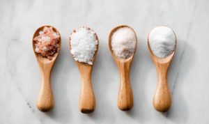 Various salt types in 4 wooden spoons on white marble.