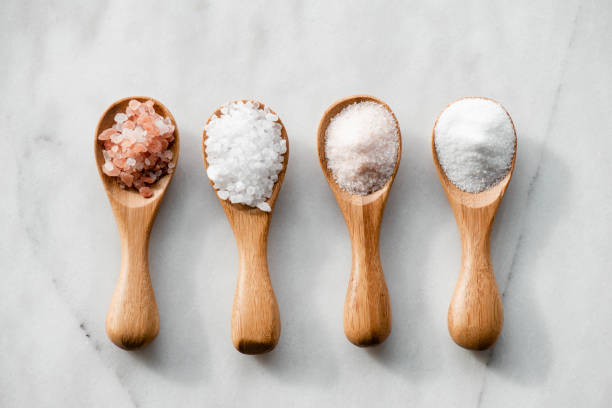 Various salt types in 4 wooden spoons on white marble.