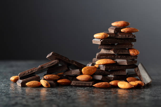 Broken dark chocolate bar with almond on a black background. Copy space.